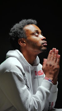 a man in a white hoodie praying in front of a black background