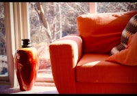 an orange couch next to a window with a vase