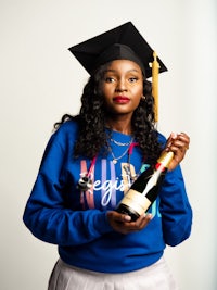 a young woman in a graduation cap and gown holding a bottle of champagne